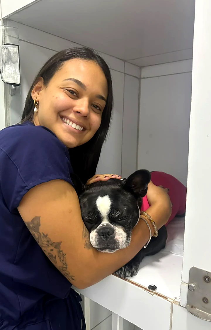Colaboradora sorrindo e abraçando um buldogue francês preto e branco