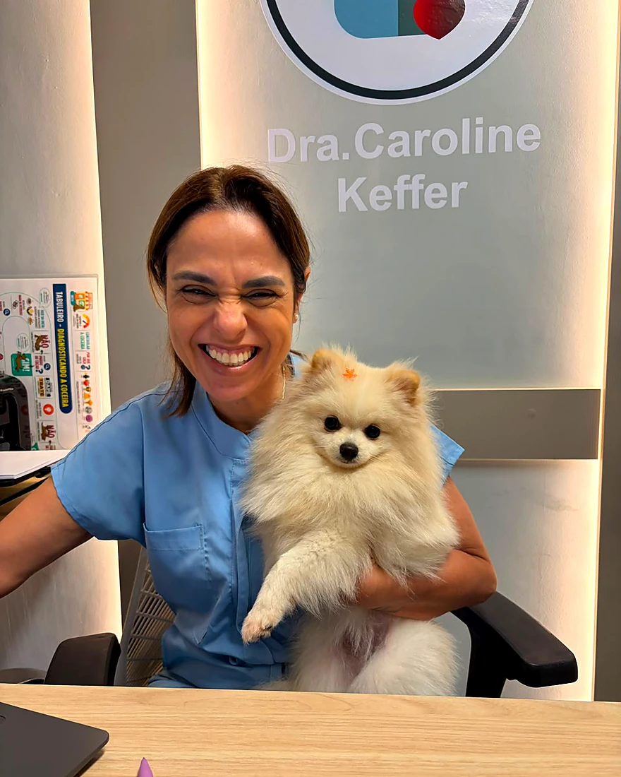 Dra. Caroline Keffer sorrindo no consultório com um lulu da pomerânia no colo