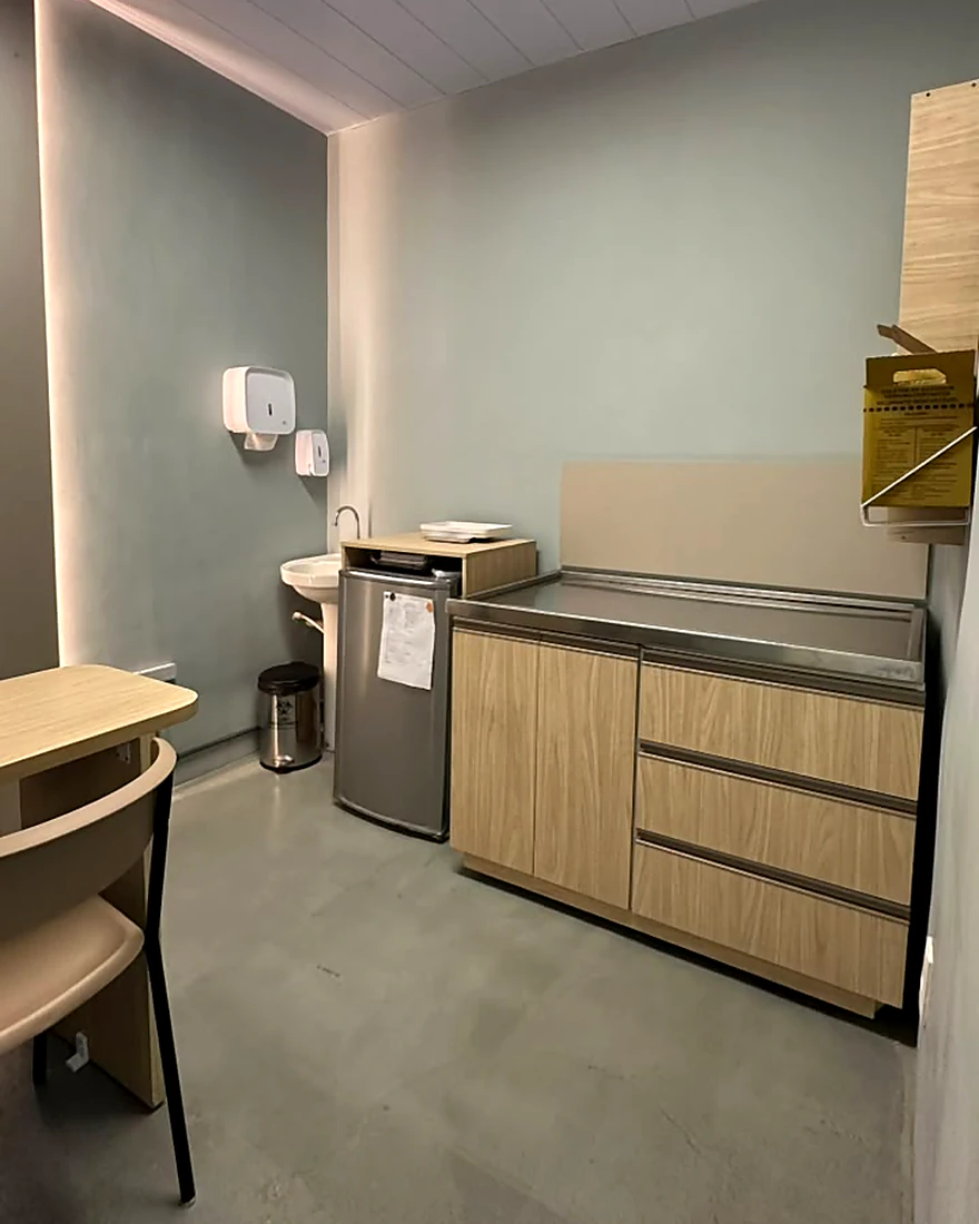 Consultório da clínica com bancada de exame em inox, pia e armários