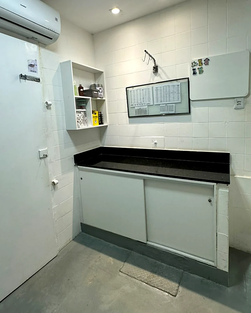 Laboratório da clínica, com bancada de granito, tabela de referência na parede e material de coleta